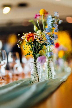 Şarap kadehleri ve çiçekli yemek masası, düğün için mükemmel, zarif bir parti ya da açık hava kutlaması için. Sıcak ışıklar ve yumuşak bokeh samimi ve lüks bir atmosfer yaratır..