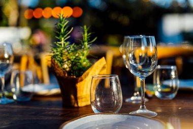 Şarap kadehleri ve çiçekli yemek masası, düğün için mükemmel, zarif bir parti ya da açık hava kutlaması için. Sıcak ışıklar ve yumuşak bokeh samimi ve lüks bir atmosfer yaratır..