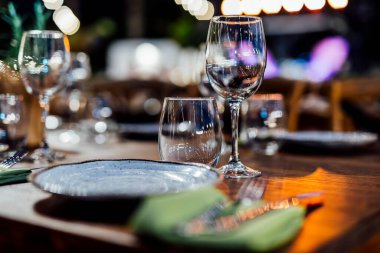 Şarap kadehleri ve çiçekli yemek masası, düğün için mükemmel, zarif bir parti ya da açık hava kutlaması için. Sıcak ışıklar ve yumuşak bokeh samimi ve lüks bir atmosfer yaratır..