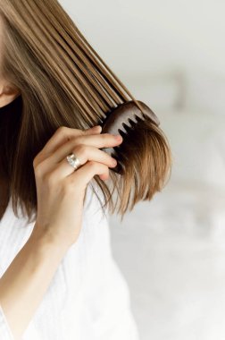 a beautiful girl in a white coat smiling combs her hair with an ecological comb