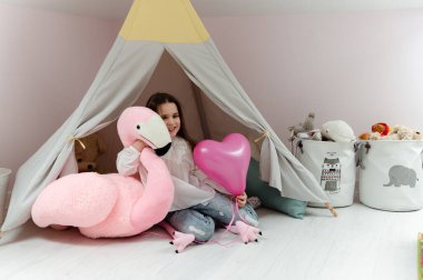 Genç bir kız odasında yumuşak pembe bir flamingoyla bir çadır ve odanın içinde oynuyor. çocuk odası