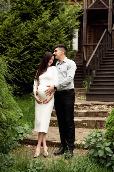 結婚した夫婦は木の生態系の家を背景に優しく抱きつく 妻は妊娠してる 妊娠中の女性を優しく抱きかかえて — ストック写真