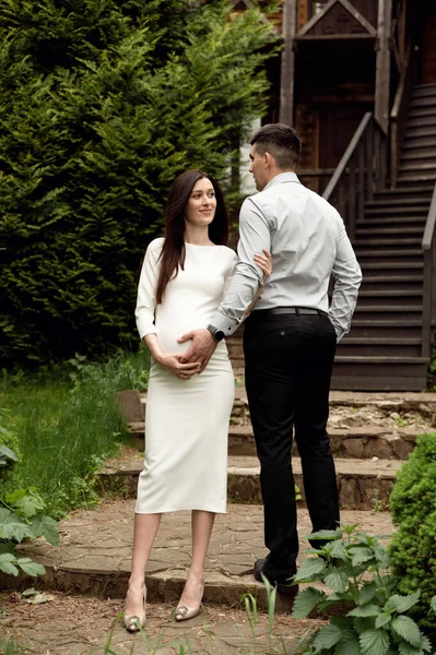 結婚した夫婦は木の生態系の家を背景に優しく抱きつく 妻は妊娠してる 妊娠中の女性を優しく抱きかかえて — ストック写真