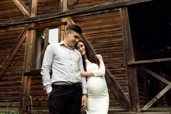 森の木造生態系の家を背景に美しい妊娠中のカップル 妊娠中の女性を抱きかかえて — ストック写真