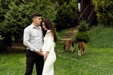 Doğada hamile bir çiftin güzel bir portresi. Kocası hamile karısına sarılıyor.