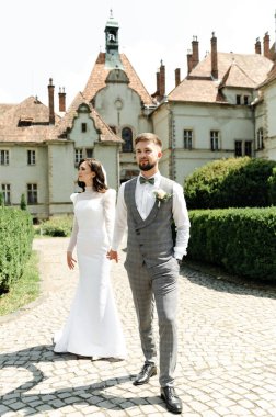 Güzel bir çift yeni evli şatoya doğru yürür. Gelin ve damat kalenin dışındayken el ele tutuşuyorlar. düğün kavramı.