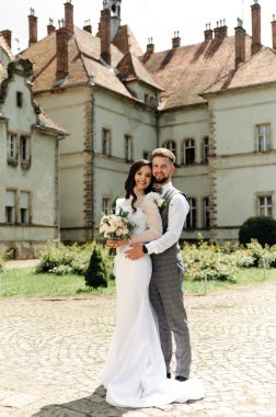 Yeni evliler yazın kalenin bölgesindeyken birbirlerine sarılıyorlar. Genç gelin ve sakallı damat dışarıda sarılıyor..