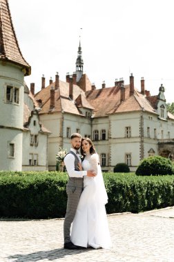 Yelek giymiş sakallı damat gelinle yürüyor. Yeni evlilerin güzel şatoya bakan düğün yürüyüşü..