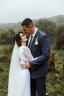 Uzun boylu damat ve kısa boylu gelin. Sonbaharda yeni evlilerin düğün günü. Çift şefkatle sarılıyor. Avrupa görünüşü. büyümedeki fark