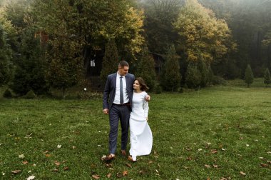 Sonbahar sezonunda genç bir çift açık havada evleniyor. Sonbahar düğünü. boy farkı. Damat gelini kucaklıyor. Sis ve düşen yaprakların arka planında yeni evliler.