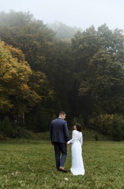 Sonbahar parkında düğün yürüyüşü. Boyları farklı olan yeni evliler. Törenden sonra evlenen çift. Çift el ele tutuşuyor..