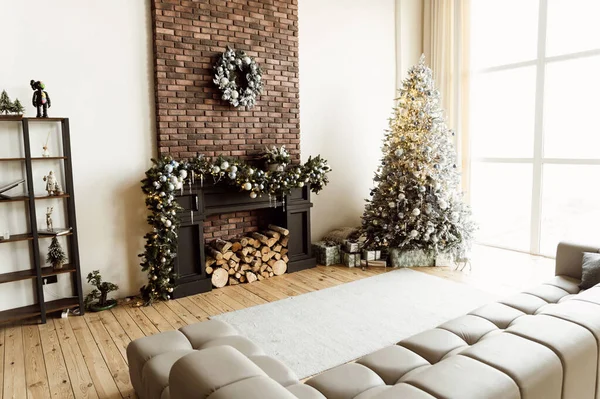 beautiful christmas room with fireplace and sofa and large window. festive mood in anticipation of Christmas. There is a Christmas tree with gifts in the room.