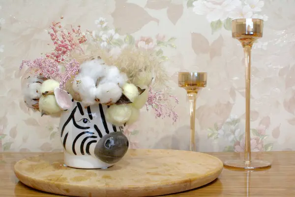 vase of flowers on the table in the room. Glass candlesticks, vintage wallpaper on the wall. vase in the shape of a zebra. dried flower