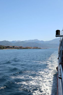 Güneşli bir günde arka planında dağlar olan hareket halindeki bir tekneden sahil kasabası manzarası. Boka Kotorska Körfezi, Kotor Körfezi. Karadağ. Körfez etrafında gezinti.