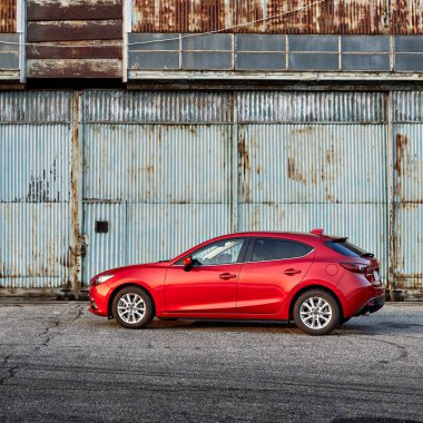 Eski bir uçak hangarının önüne park edilmiş kırmızı bir Mazda 3. Mazda 3 2013-2019 'da üretildi. Katowice - Polonya, 15 Şubat 2015