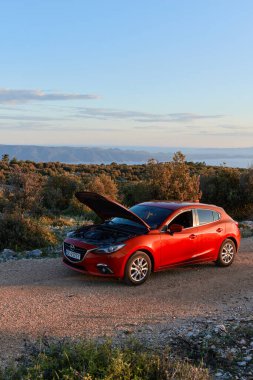 Kaputu açık kırmızı Mazda 3, bir ada turu sırasında ayakta duruyor. Gün batımı, insan yok. Brac Adası, Hırvatistan - 05.31.2019