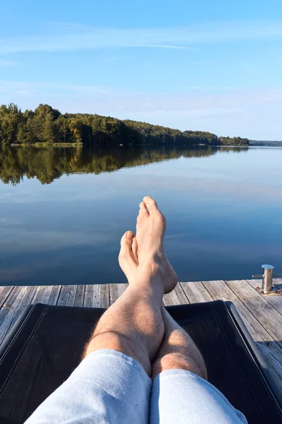 The legs of a man lying on a deck chair at the lake pier