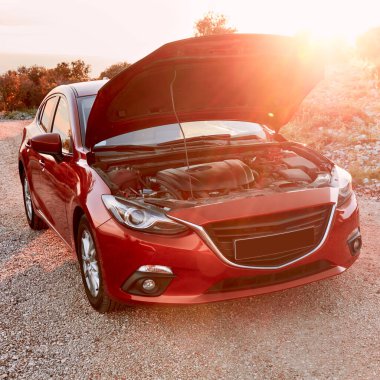 Kaputu açık kırmızı bir araba Akdeniz 'de bir tatil gezisinde duruyor. Yakıt yok, akü ya da motor arızası yok. Çerçevede gün batımı ve insan yok..