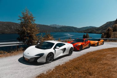 Road trip with supercars. Mclaren 650s, Ferrari F12 and Lamborghini Huracan parked on a gravel road by the lake. Gransherad, Norway. 04.06.2016 clipart