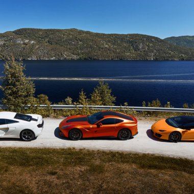 Beyaz Mclaren 650 'ler, kırmızı Ferrari F12 ve sarı Lamborghini Huracan göl kenarındaki çakıllı yolda park etmiş. Gransherad, Norveç. 04.06.2016
