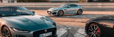 Üç Jaguar F tipi modern ofis binasının arka planında duruyor. Aracın ön tarafına yakın çekim. Katowice, 17 Haziran 2022