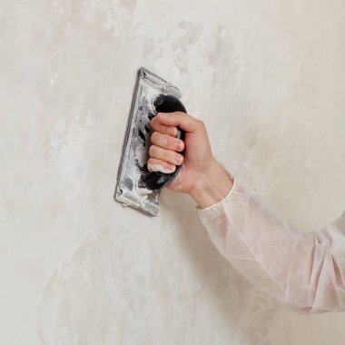 Sıvayı sıktıktan sonra duvarı zımparalayan bir adamın eli.