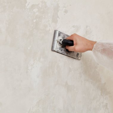 Sıvayı sıktıktan sonra duvarı zımparalayan bir adamın eli.