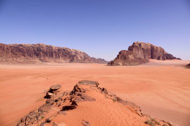 Ürdün 'deki Wadi Rum' un dramatik çöl manzarası. Uçsuz bucaksız kum ovaları ve yüksek kumtaşı dağları. Sıcak öğleden sonra ışığında doğal kaya oluşumları