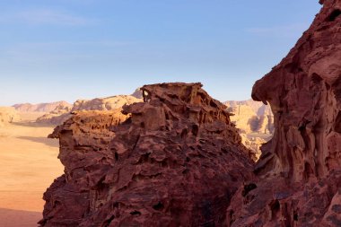Wadi Rum Çölü 'nde dramatik kırmızı kaya oluşumları, Jordan. Rüzgâr ve zamanla şekillenen antik kumtaşı kayalıkları parlak mavi gökyüzünün altında çarpıcı bir jeolojik manzara yaratır.