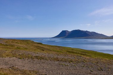 İzlanda 'da dağ ve fiyortlu dramatik kıyı manzarası. Saf mavi su, engebeli araziyle birleşir. Seyahat yeri, İskandinav doğası ve vahşi doğa manzarası..