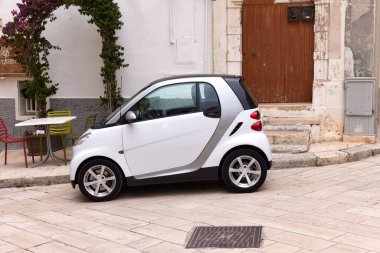 Tarihi merkeze park edilmiş beyaz bir Smart ForTwo. Mikro araba, Puglian kasabasındaki bu resim gibi manzaradaki antik taş mimari ile çelişiyor. 25.06.2022, Monopoli, İtalya