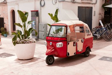 Beyazlatılmış binanın önüne park edilmiş klasik kırmızı bir Piaggio Ape. Tepesi tuvalden yapılmış geleneksel üç tekerlekli kullanım aracı. 25.06.2022, Monopoli, İtalya