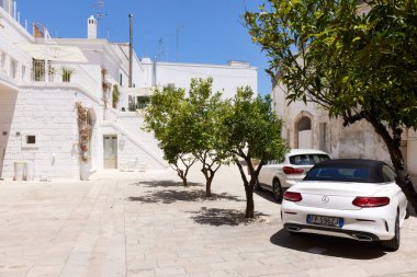 Beyaz bir Mercedes-Benz C-Sınıfı üstü açık araba turunçgilli bir avluya park edilmiş. Lüks Alman arabası tarihi mimariye karşı çarpıcı bir tezat oluşturuyor. 26.06.2022, Monopoli, İtalya