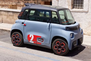 Açık mavi Citroen Ami marka bir mikro araba sokağa park edilmiş. Bu küçük elektrikli kuadrisiklet, antik Akdeniz kent ortamının aksine modern şehir hareketliliğini temsil etmektedir. 26.06.2022, Monopoli, İtalya