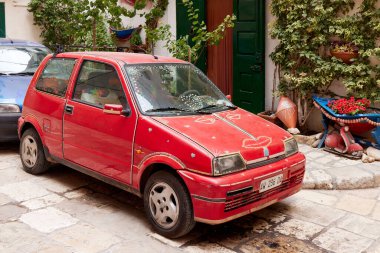 İtalya 'nın Monopoli kentindeki tırmanma tesislerinin bulunduğu pitoresk bir avluya park edilmiş süslü kırmızı bir Fiat 500. İkonik İtalyan kompakt arabası boncuklu süslemeler içerir. 25.06.2022, Monopoli, İtalya