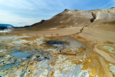 Hver, İzlanda. Turistler, İzlanda 'da doğal bir bölgede kaynayan çamur çukurları ve canlı mineral bölgeleri de dahil olmak üzere eşsiz jeotermal özellikler arasında yürürler..