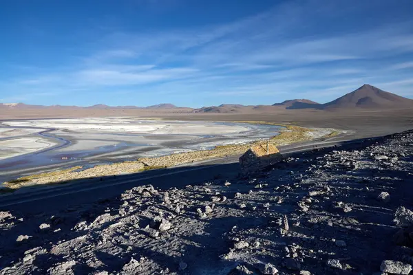 Altın güneş ışığı, Avaroa Ulusal Parkı 'nın eşsiz tuz düzlüklerine gölge düşürürken uzak dağlar, sakin mavi gökyüzüne doğru yükseliyor ve nefes kesici bir doğal manzara yaratıyor..