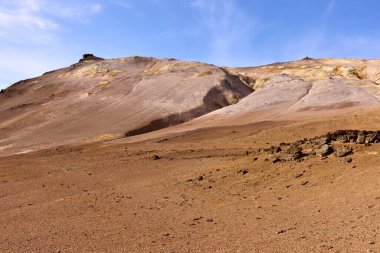 Hver, İzlanda. Kuru ve çorak bir arazi, güneş ışığını yansıtan eğimli tepelerle çarpıcı jeolojik oluşumlara sahiptir. Arazi toprak tonları açısından zengin, bu da erozyonu gösteriyor.