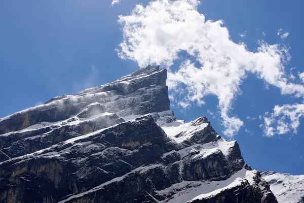 Yürüyüşçüler Annapurna yolunda ilerlerken, parlak mavi bulutlarla yükselen kaya oluşumları gibi. Kar örtüsü engebeli arazinin bazı kısımlarını kaplıyor