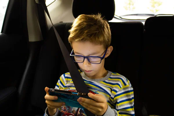Çocuk bir arabanın arka koltuğunda akıllı telefonuyla oynuyor.