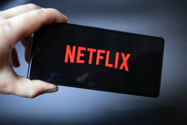 Netflix logosu olan bir akıllı telefonu tutan el.