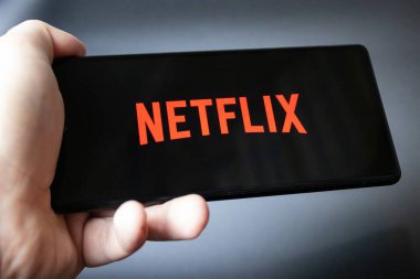 Netflix yayın servisi logosu olan bir akıllı telefonu tutan el.