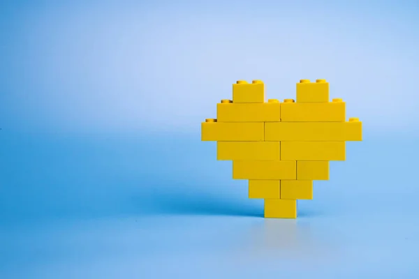 Mavi arka planda plastik yapı taşlarından yapılmış sarı kalp