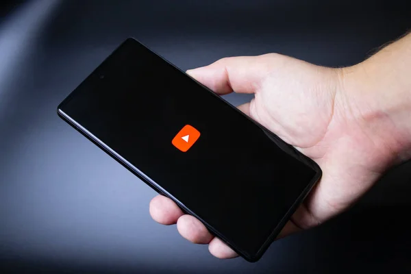 Üzerinde youtube logosu olan bir akıllı telefonu karanlık arka planda tutmak.