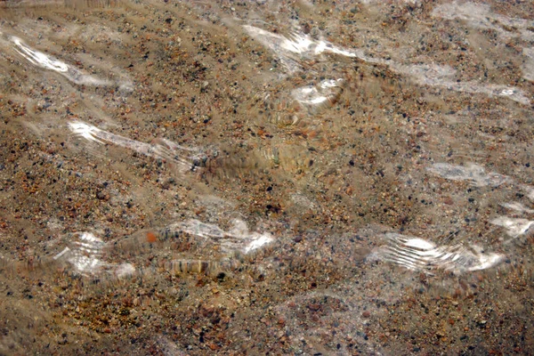 Altında küçük kayalar ve kum olan kusursuz berrak bir su.