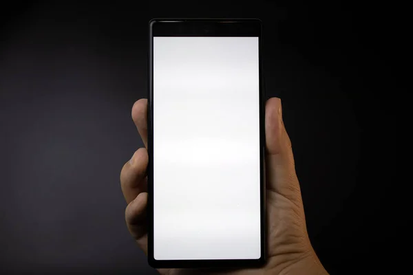 Bir el, arka planda beyaz ekranlı bir akıllı telefonu gösterir