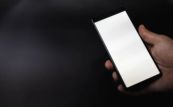 Gri siyah arka planda beyaz ekranlı akıllı telefonu gösteren bir el.