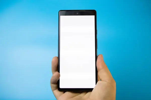 Mavi arka planda beyaz beyaz ekranlı akıllı telefonu tutan bir el.
