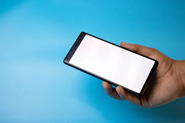 Bir el mavi arkaplanda beyaz boş ekranlı bir akıllı telefonu gösterir