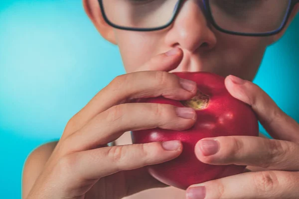 Domates tutan gözlüklü bir çocuğun yakın plan fotoğrafı.